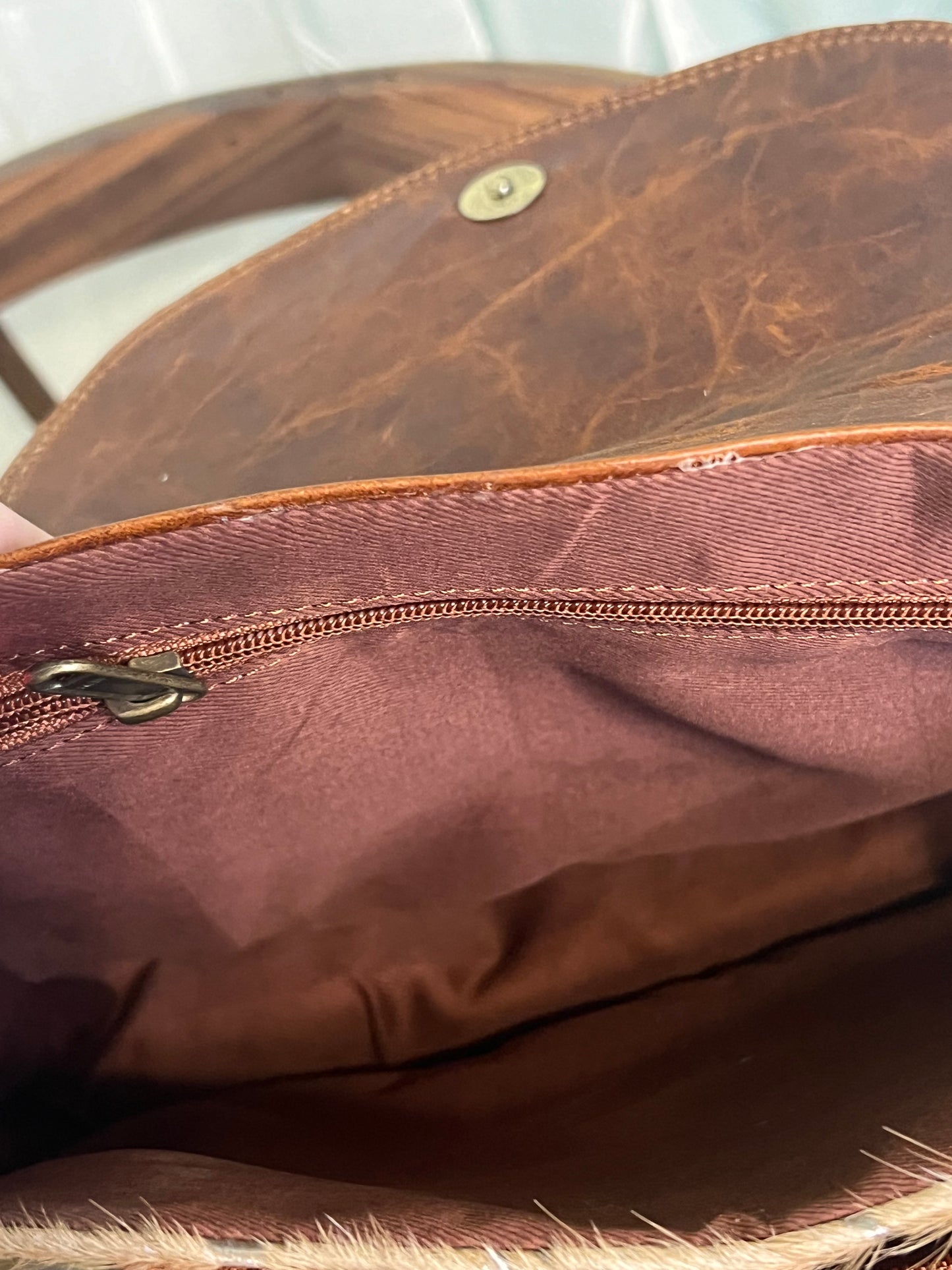 Falls City Bag by Crazy Heifers – handmade leather and cowhide bag with silver splatter design, adjustable strap, zippered front pocket, and magnetic snap closure.