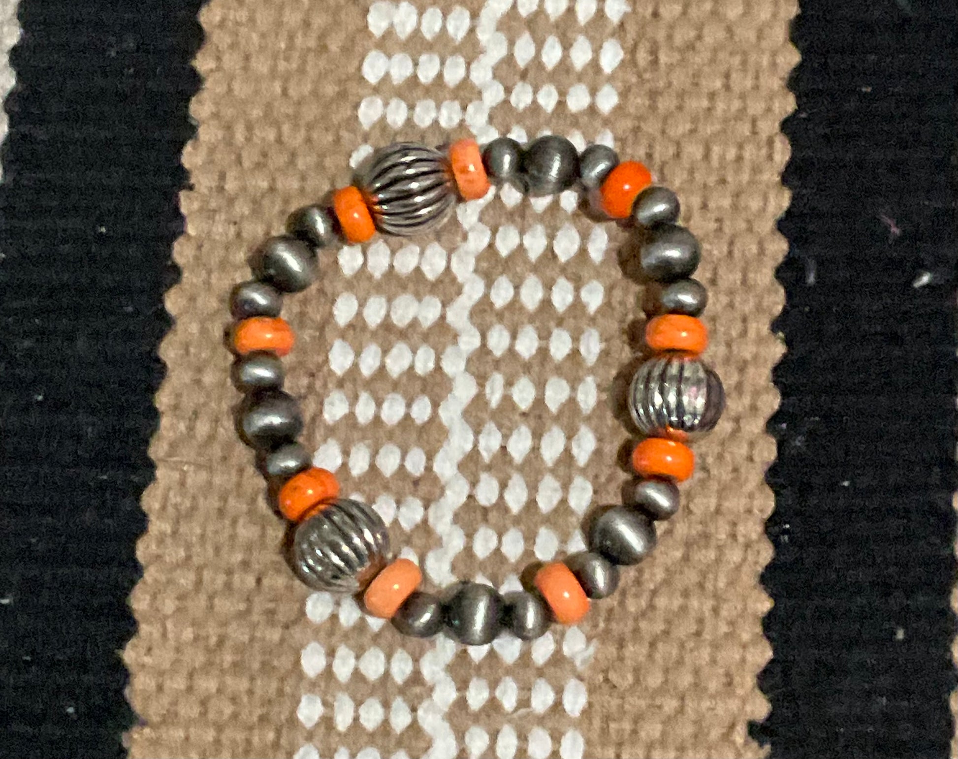 The Desert Drift Stretch Bracelet featuring a mix of warm faux silver and rich orange stone beads, styled on a neutral background with rustic, earthy textures.