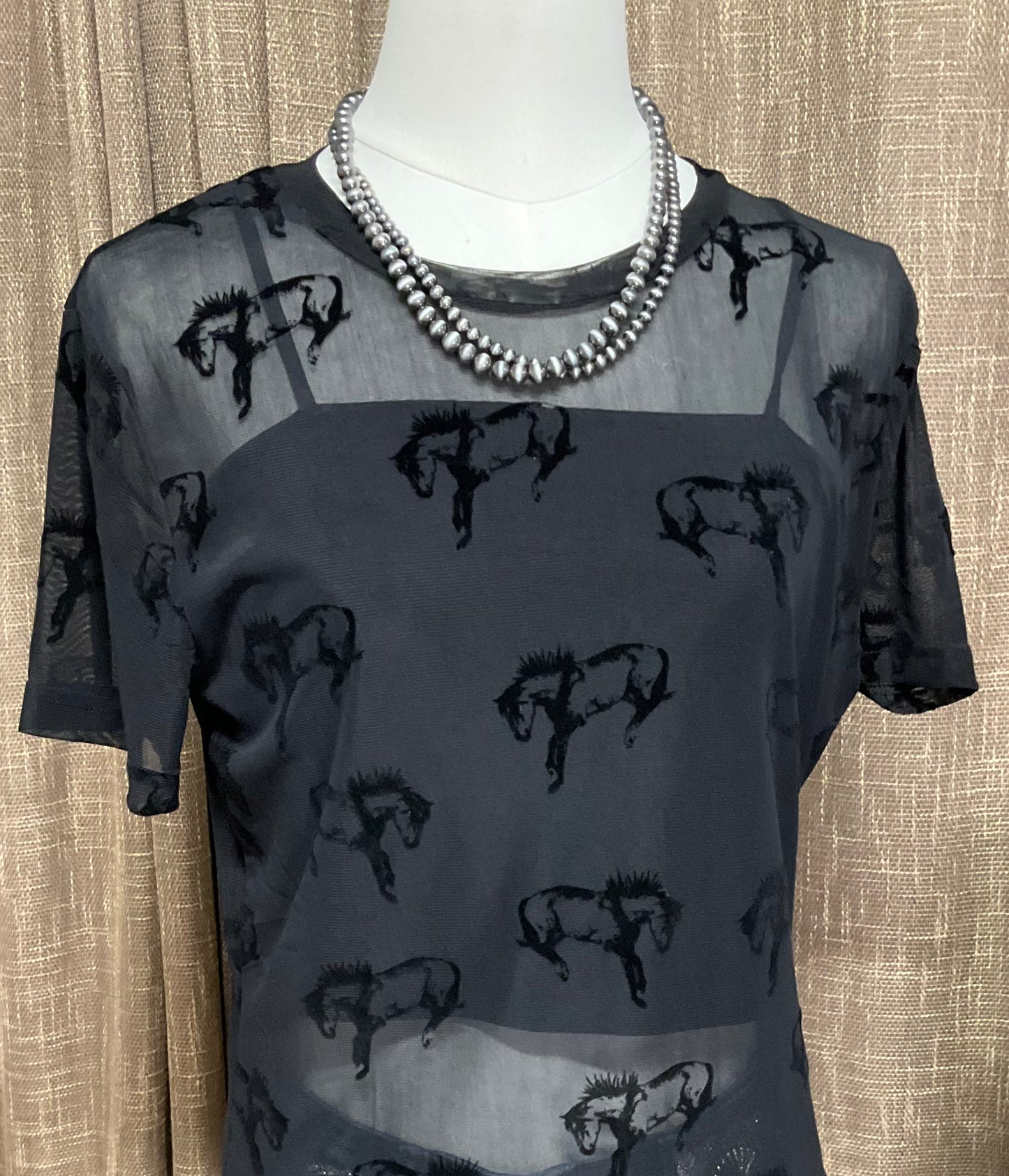Close-up image of the Buck Off Mesh Tee showcasing a bold bucking horse pattern on a short-sleeve, stretchy fabric design, paired with an included cami for a complete, edgy look.