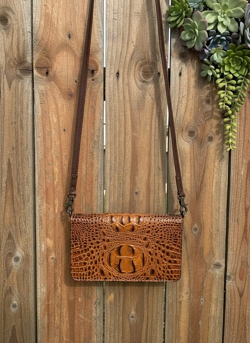 Brown leather handbag with crocodile texture on a wooden surface with succulents.