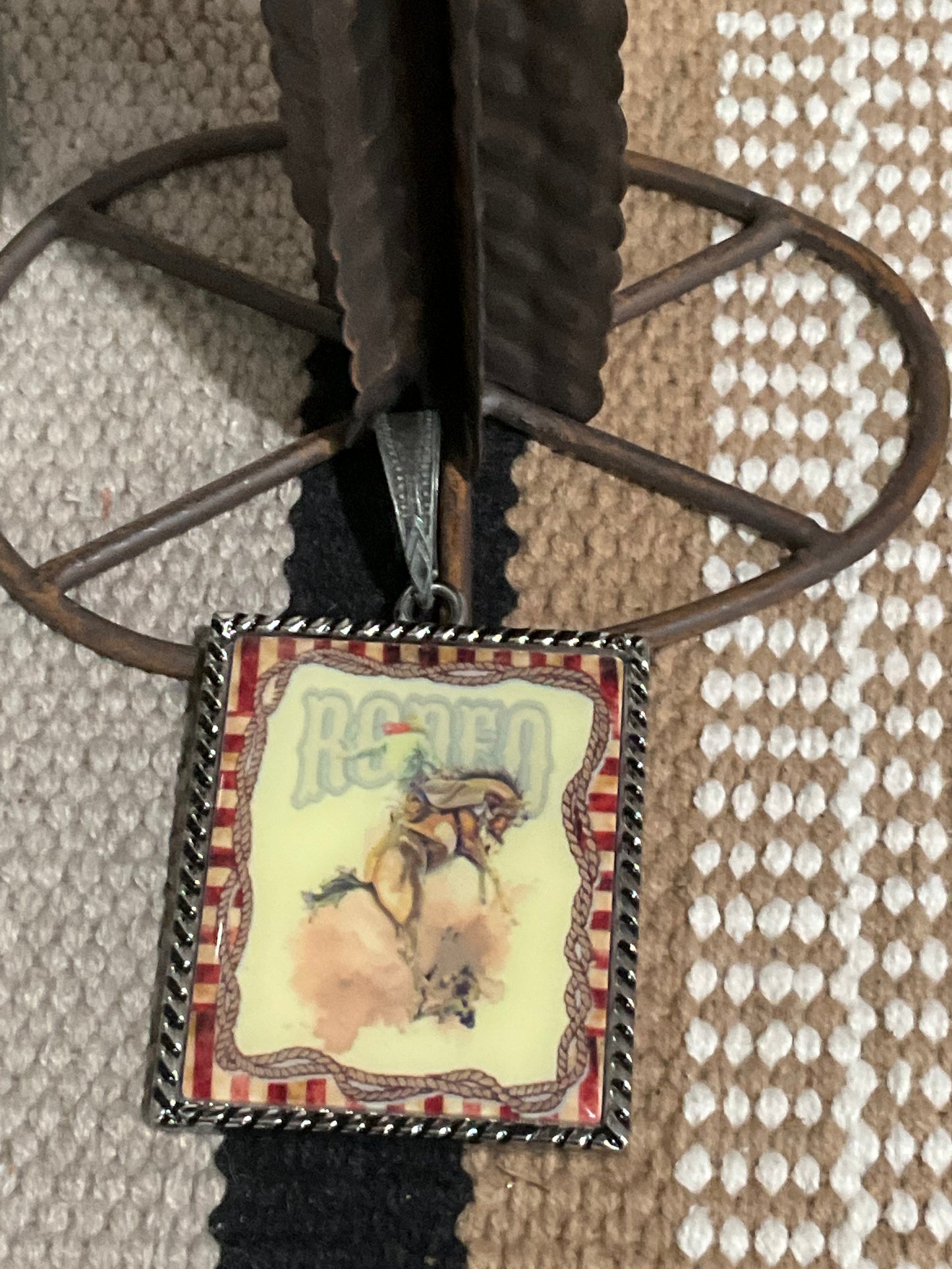 Close-up of The Buckle Up Pendant, a bold 3-inch pendant featuring a vintage rodeo poster design. This statement piece is shown ready to slide onto a strand of pearls or chain, capturing a nostalgic western vibe.