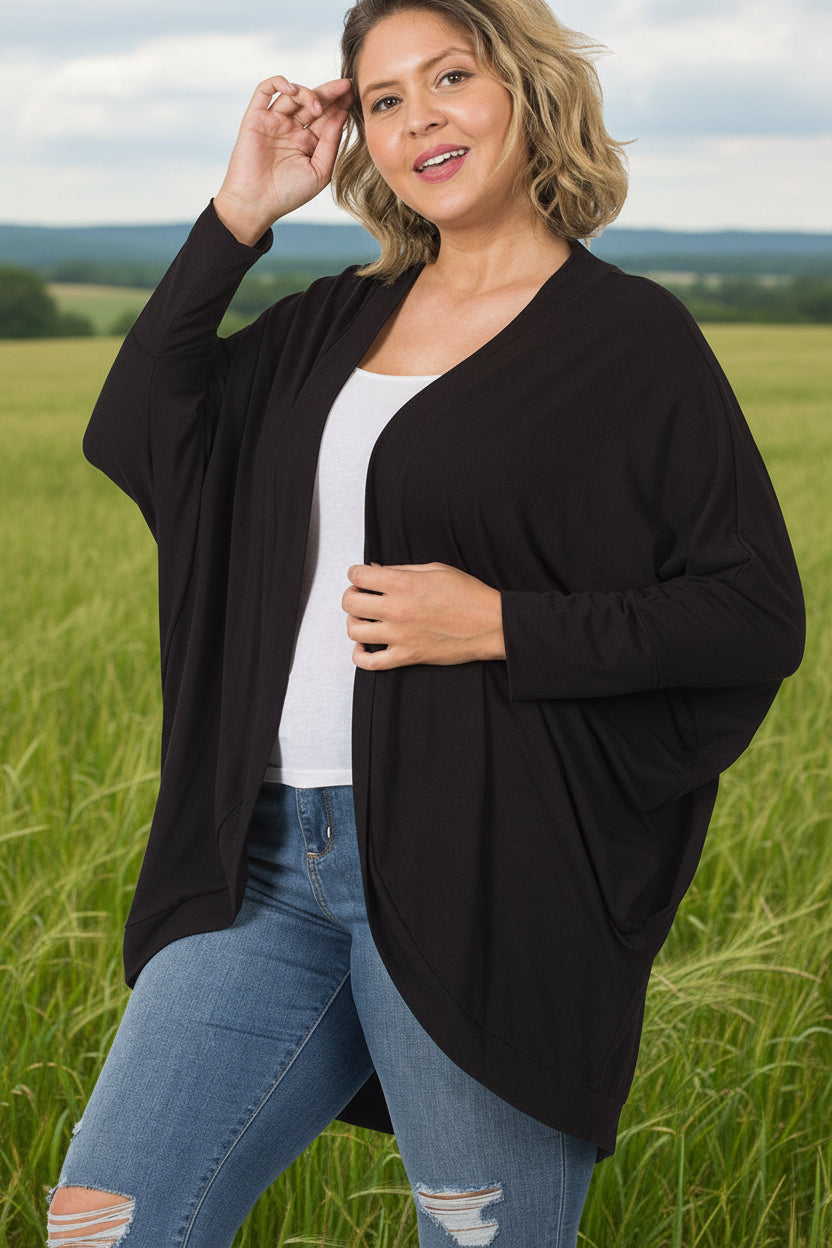 Model wearing a relaxed-fit cocoon wrap cardigan with a soft, draped silhouette. Lightweight, stretchy knit fabric shown layered over a tee and jeans for a cozy, casual outfit.