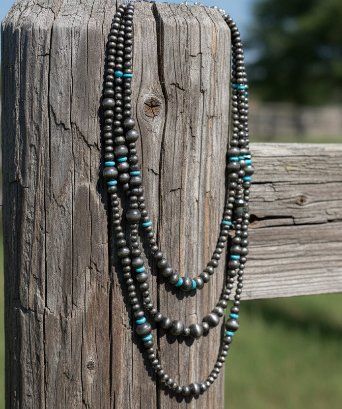 Triple strand silver-tone beaded necklace with turquoise-colored rondelle accents and layered western style.