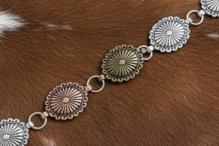 Mixed metal oval concho belt with bronze, copper, and silver-tone finishes and adjustable chain extender.