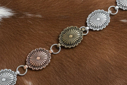 Mixed metal oval concho belt with bronze, copper, and silver-tone finishes and adjustable chain extender.