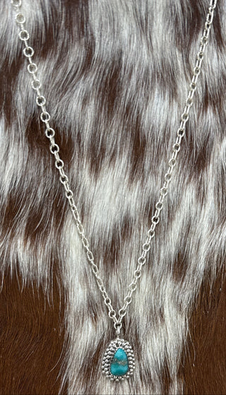 Handmade sterling silver genuine turquoise teardrop pendant necklace displayed on brown and white cowhide