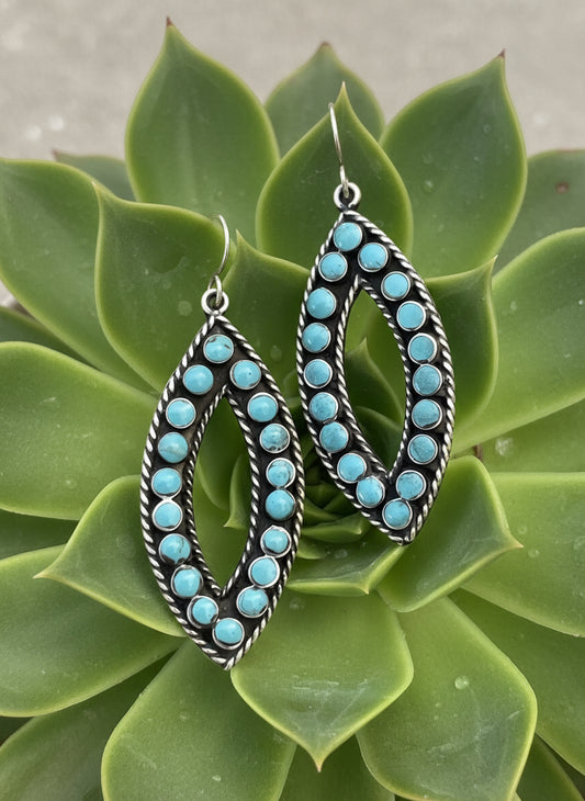 Panola Sterling Earrings featuring marquise-shaped sterling silver frames with turquoise dot inlay and rope edging, displayed on succulent background
