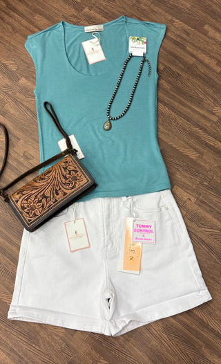 Flat lay of white Risen tummy control shorts paired with a teal scoop neck top, turquoise stone pendant necklace, and tooled leather crossbody bag. Displayed on a rustic wood background.