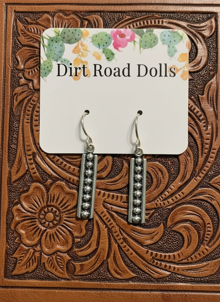 Ross Sterling Earrings featuring vertical sterling silver bars with raised silver pearl accents on oxidized background, displayed on tooled leather