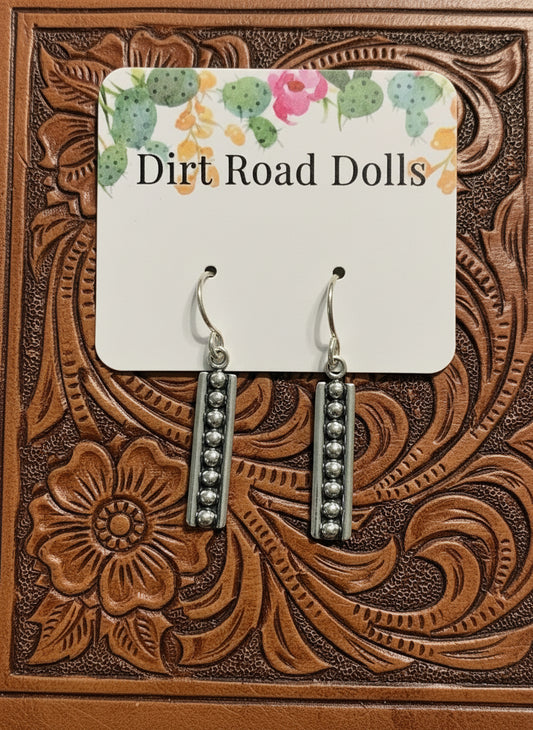 Ross Sterling Earrings featuring vertical sterling silver bars with raised silver pearl accents on oxidized background, displayed on tooled leather