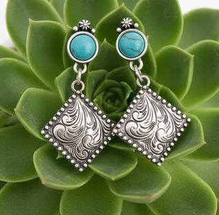 Silver-tone western dangle earrings with turquoise-style stud tops and engraved scroll diamond-shaped drops, approximately 2 inches long.