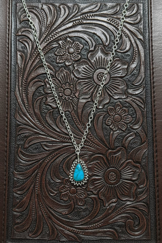 Handmade sterling silver teardrop necklace with genuine turquoise stone and double beaded border displayed on tooled leather