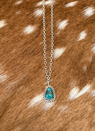 Handmade sterling silver turquoise teardrop pendant necklace displayed on brown axis hide