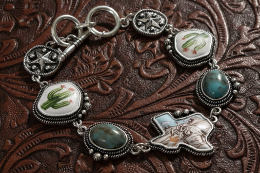Silver-tone western charm bracelet with turquoise-style stones, engraved details, painted cowboy and cactus scenes, and toggle closure.
