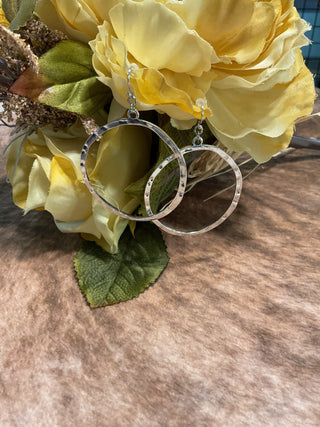 Silver-tone hammered open hoop earrings on French hooks displayed in front of yellow flowers; lightweight modern design