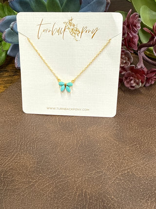 Handmade Kingman turquoise bow necklace with authentic blue turquoise stones and gold plated sterling silver chain displayed on styled jewelry background