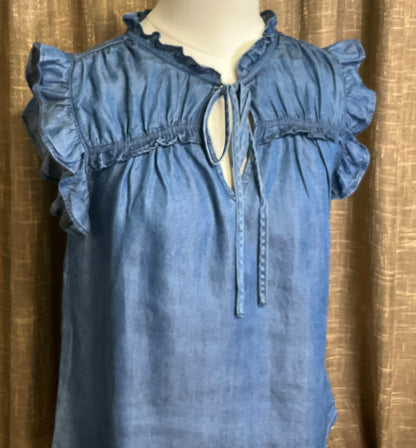Jenna Chambray Blouse in soft blue lyocell—sleeveless top with high neckline, feminine neck tie, keyhole front detail, ruffle trim, and gently ruched yoke for subtle texture and charm.