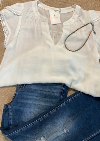 Hanna Blouse featuring a split V-neck, short petal sleeves, and delicate lace trim. Crafted from a lightweight blend of rayon, nylon, and polyester, offering a soft, flowing silhouette. Not lined.