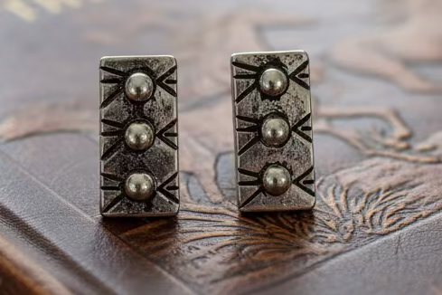Small silver-tone rectangular stud earrings with raised bead details and a western starburst textured background.
