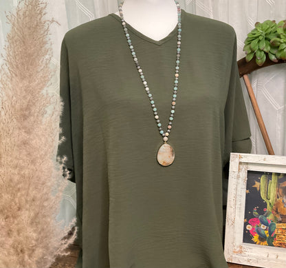 A costume jewelry necklace featuring beads in neutral, jade blue, and grey tones, accented by a polished stone pendant.