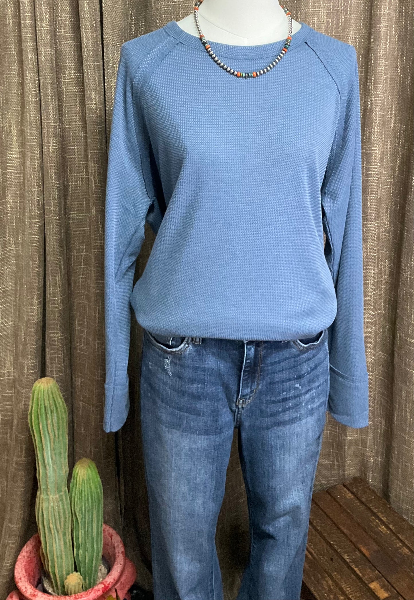 A long-sleeve waffle-knit top called the Pamela Waffle Top. It has a soft, textured fabric with a relaxed fit, a slightly rounded neckline, and subtle ribbed detailing on the cuffs and hem. The top has a casual, yet polished look, perfect for layering or wearing on its own. Ideal for creating cozy, everyday outfits.