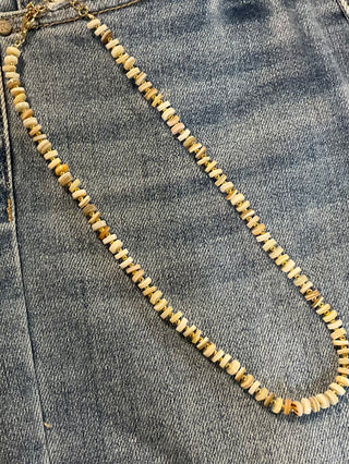A necklace with neutral-toned rondelle beads and gold-toned accents, displayed on a denim fabric.