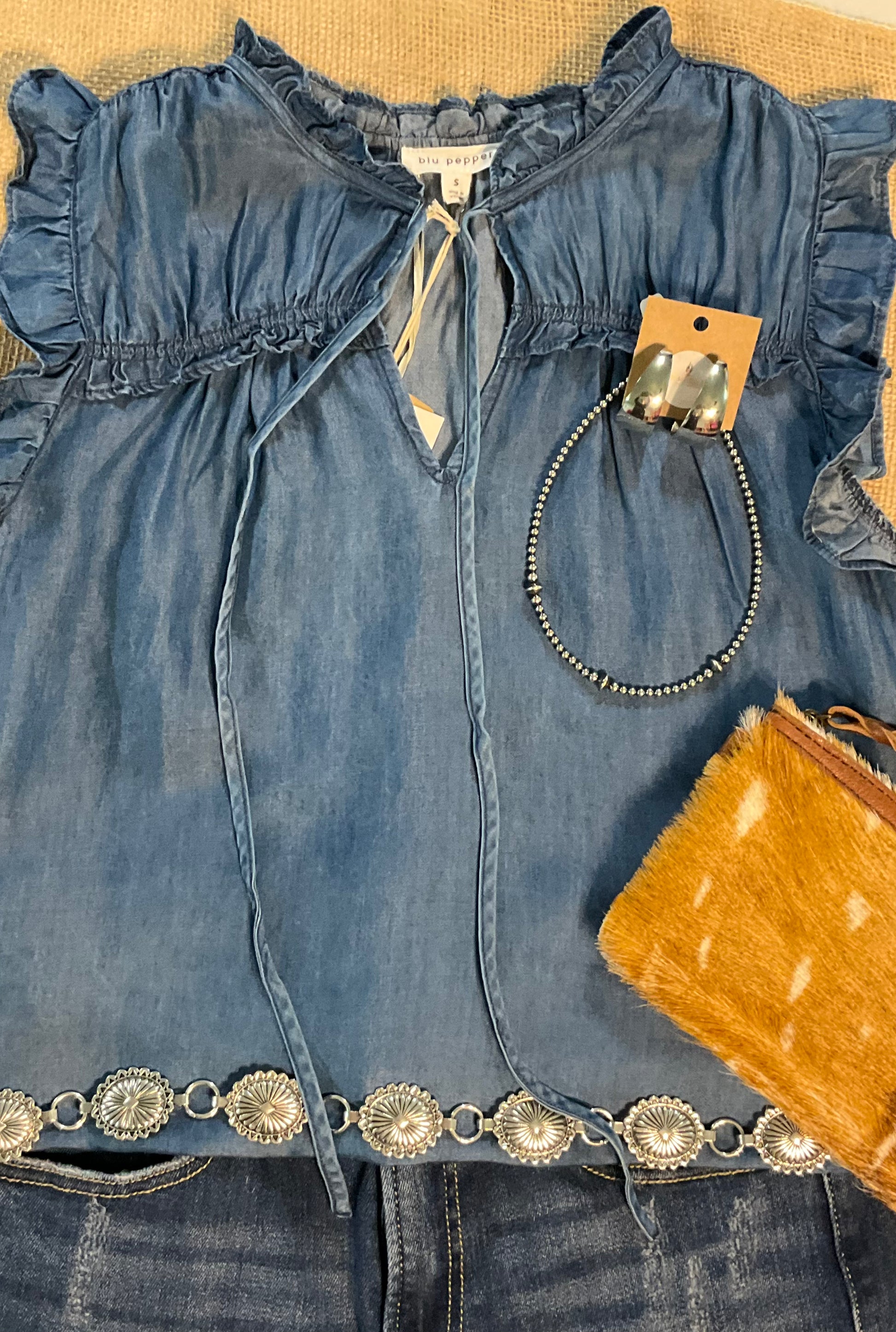 Jenna Chambray Blouse in soft blue lyocell—sleeveless top with high neckline, feminine neck tie, keyhole front detail, ruffle trim, and gently ruched yoke for subtle texture and charm.