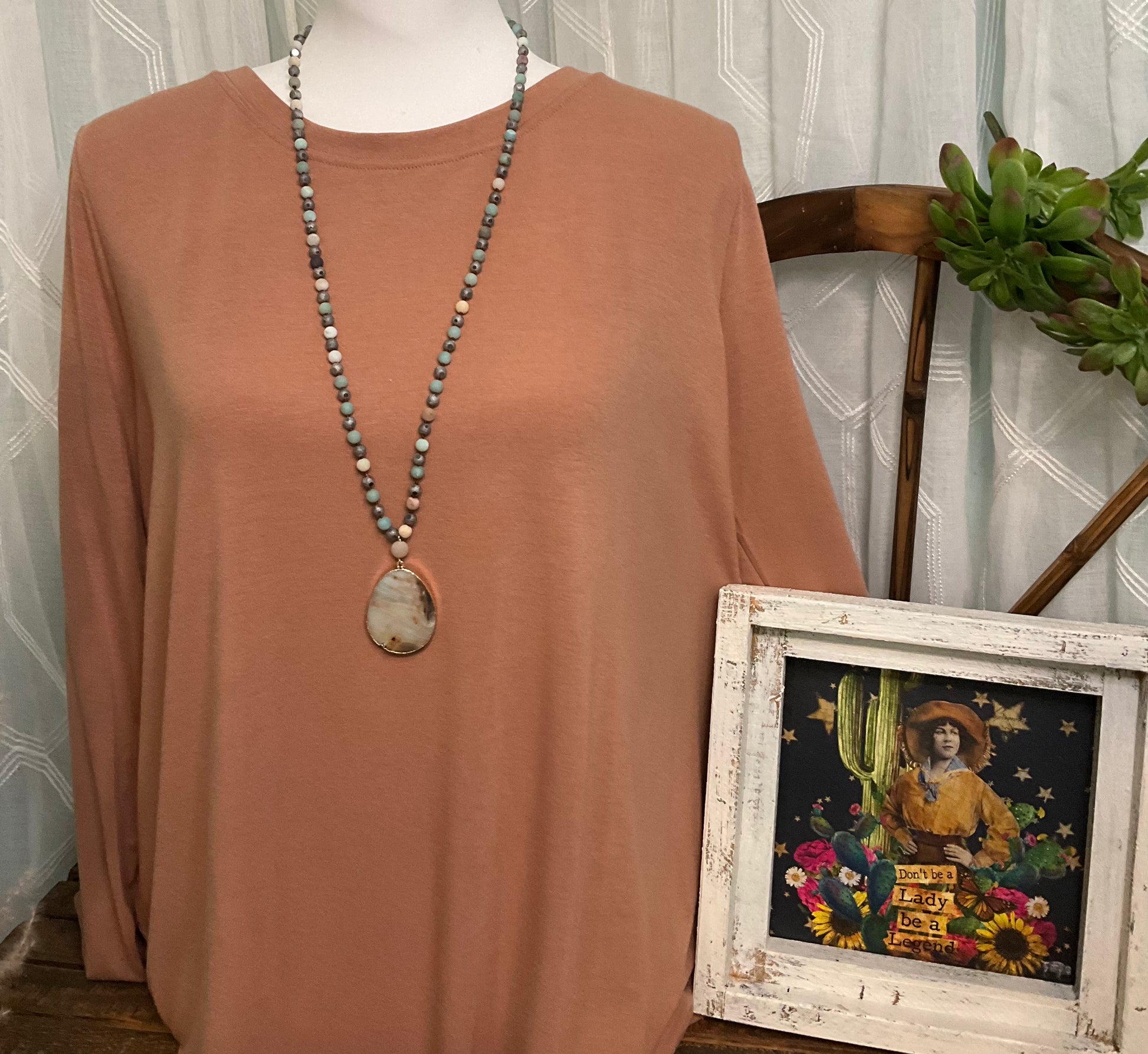 A costume jewelry necklace featuring beads in neutral, jade blue, and grey tones, accented by a polished stone pendant.