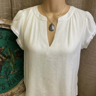 Hanna Blouse featuring a split V-neck, short petal sleeves, and delicate lace trim. Crafted from a lightweight blend of rayon, nylon, and polyester, offering a soft, flowing silhouette. Not lined.