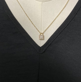 A gold-plated necklace with a dainty lock pendant featuring clear cubic zirconia stones, displayed on a mannequin wearing a black V-neck top.