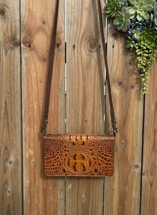 Brown leather handbag with crocodile texture on a wooden surface with succulents.