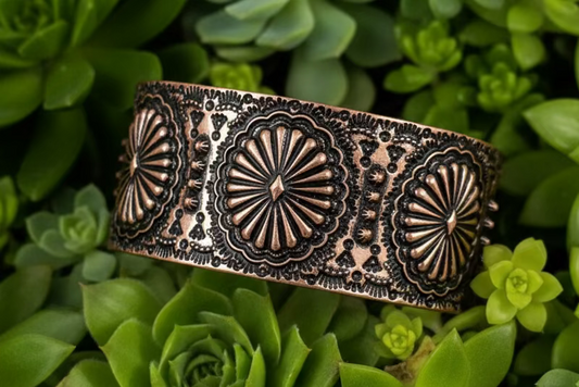 Wide western-style cuff bracelet with engraved concho designs, available in silver tone and copper tone.