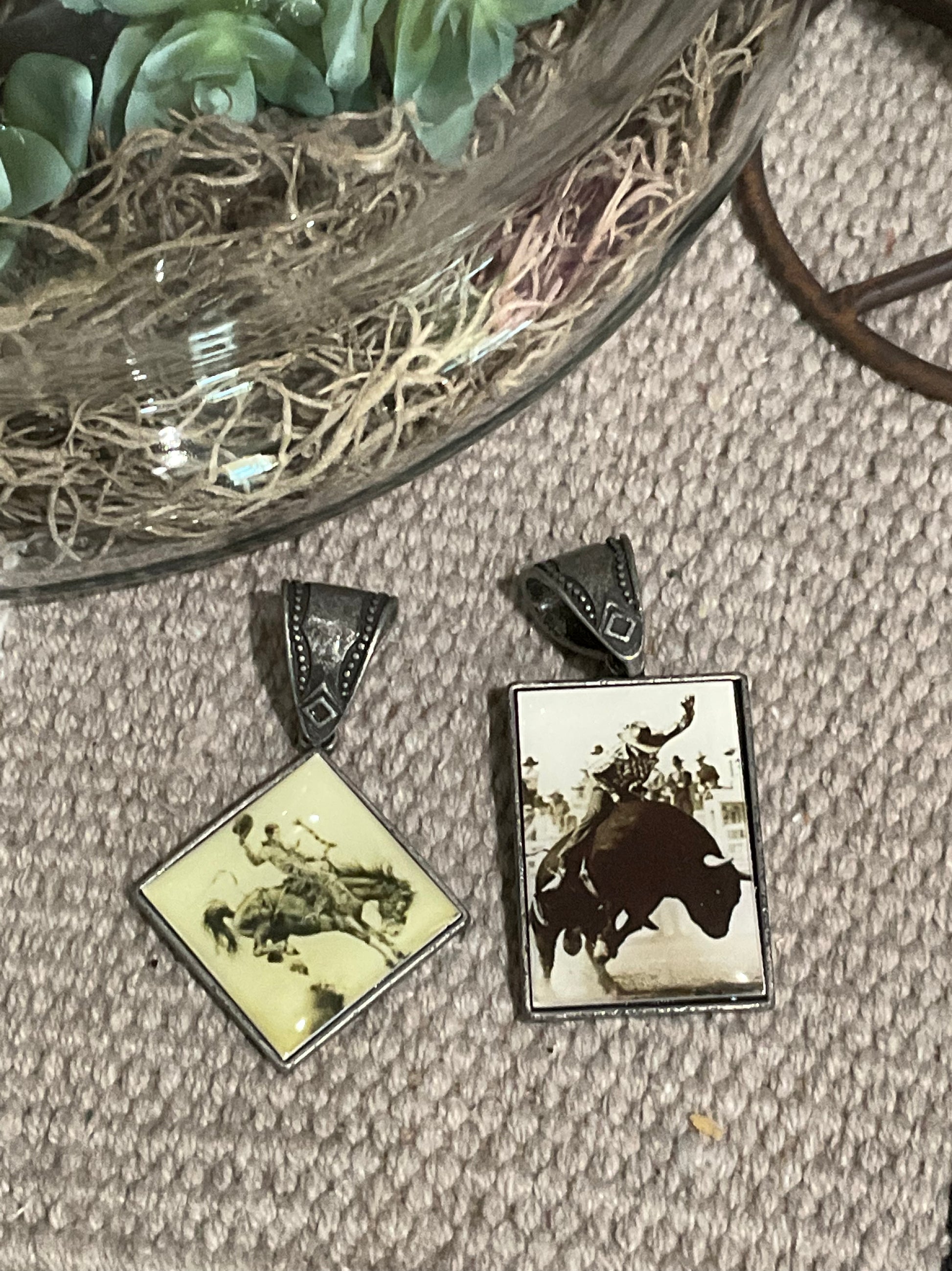 Two vintage-inspired Ranch Raised Pendants, one rectangular with a bull rider graphic and one diamond-shaped with a bronc rider design, each approx. 2” and designed to slide onto necklaces.
