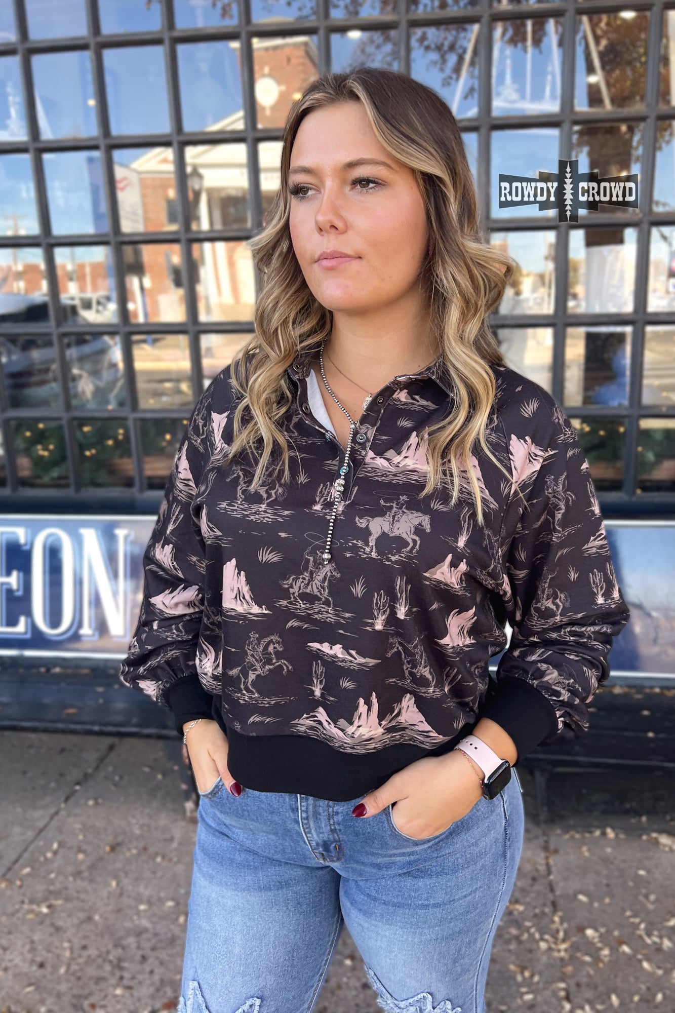 black collared long sleeve top with cream colored cowboy on horse pattern with mountains.  cuff sleeve and bottom. three turquoise snaps