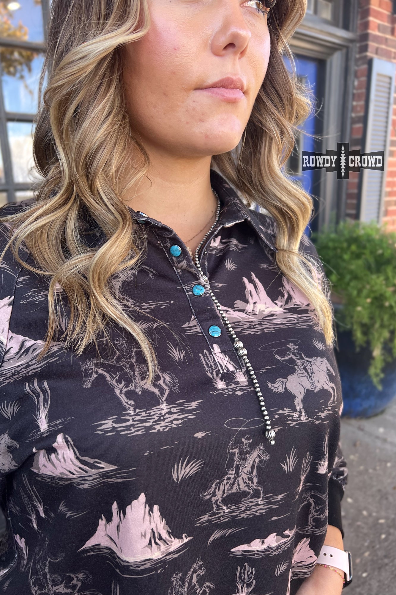 black collared long sleeve top with cream colored cowboy on horse pattern with mountains.  cuff sleeve and bottom. three turquoise snaps