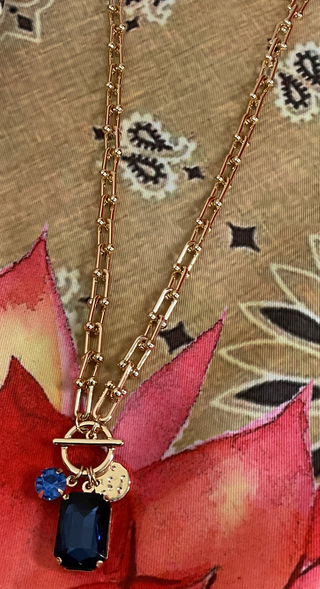 Gold charm necklace featuring emerald cut crystal and coin charm