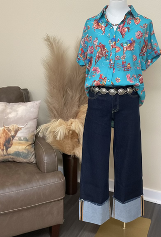 Relaxed-fit turquoise western button-up top with illustrated rodeo scene and colorful floral details.