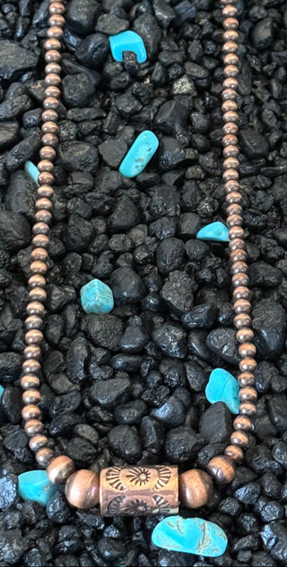 Rustic copper pearl necklace with stamped barrel focal bead displayed on black stones and turquoise nuggets