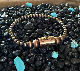 Rustic copper pearl stretch bracelet with stamped barrel focal bead displayed on black and turquoise stones