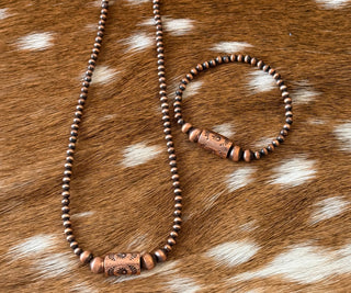 Rustic copper pearl necklace with stamped barrel focal bead paired with matching stretch copper bracelet on brown and white cowhide