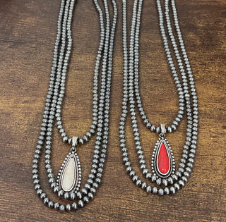 Silver toned pearl layered necklaces with faux teardrop stone pendants available in red and white