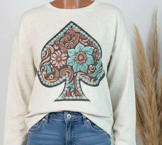 Woman wearing a white sweatshirt with a floral spade design, standing against a plain background.